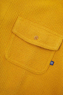 Angled mid-view of #6007 buttoned organic cotton waffle fabric short sleeve shirt in yellow with focus on button down flap chest pocket and Uskees branding tag.