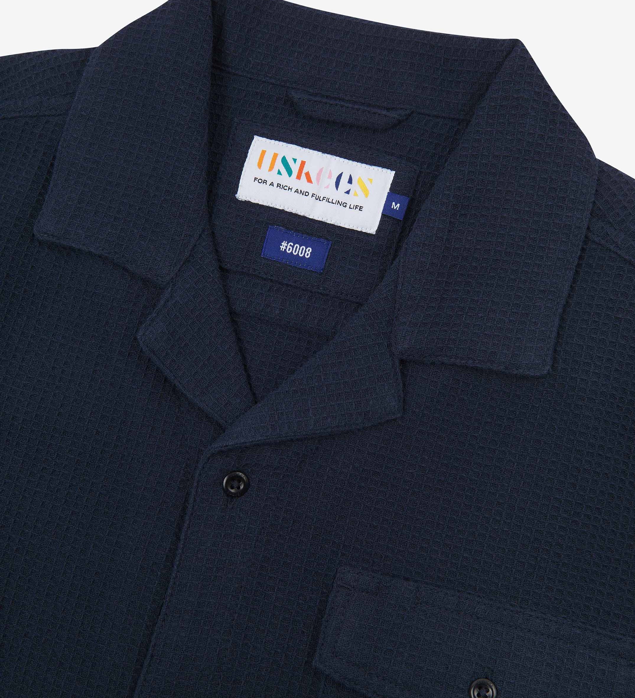 Close-up view of the #6008 shirt collar, showing weave of deep blue organic cotton waffle fabric, camp notched collar and Uskees branding label.