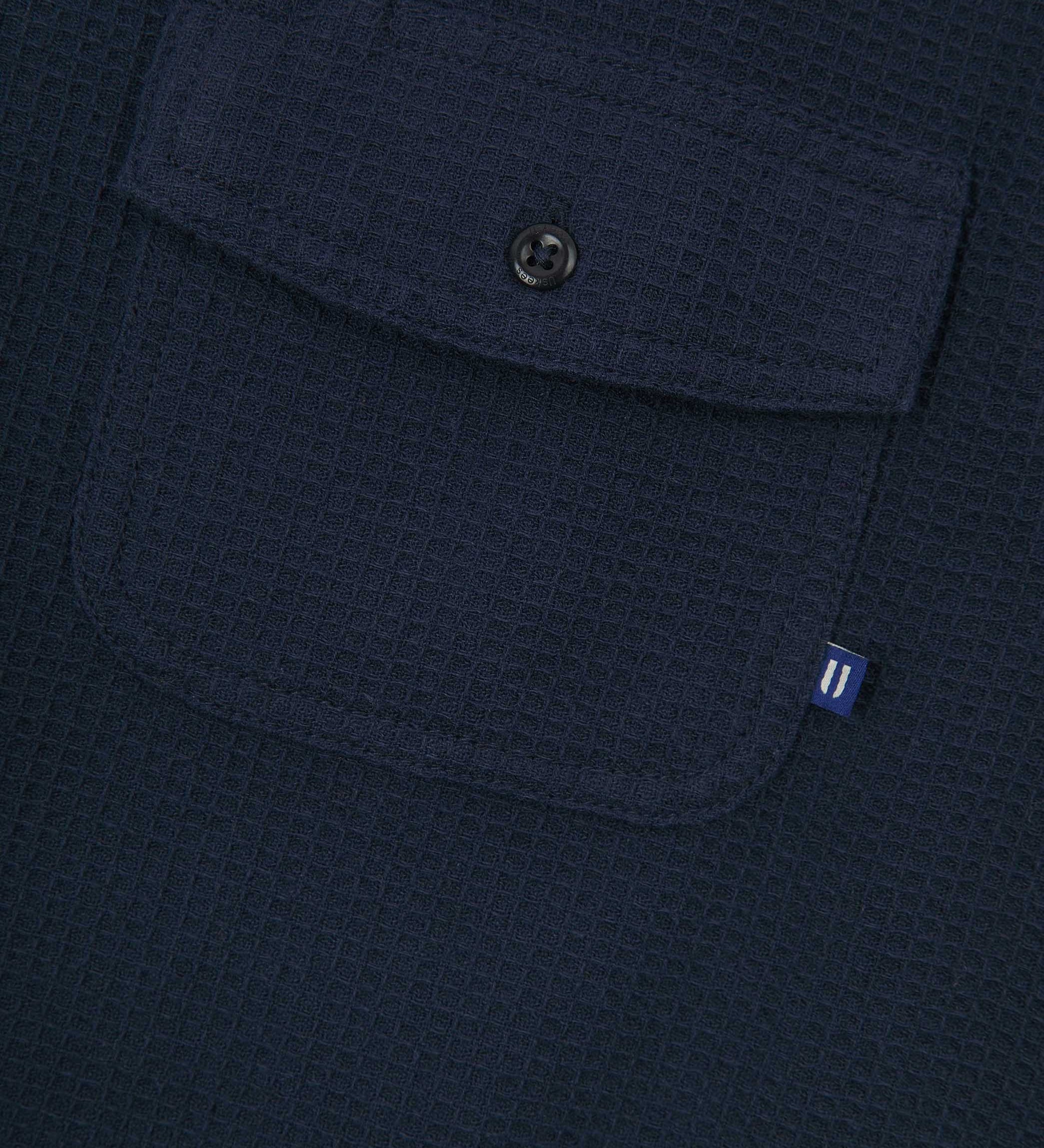 Close-up view of #6008 Uskees buttoned organic cotton waffle fabric short sleeve shirt in deep blue with focus on button down flap pocket on chest and the subtle Uskees branding tag.