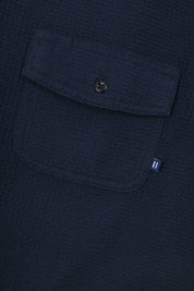 Close-up view of #6008 Uskees buttoned organic cotton waffle fabric short sleeve shirt in deep blue with focus on button down flap pocket on chest and the subtle Uskees branding tag.