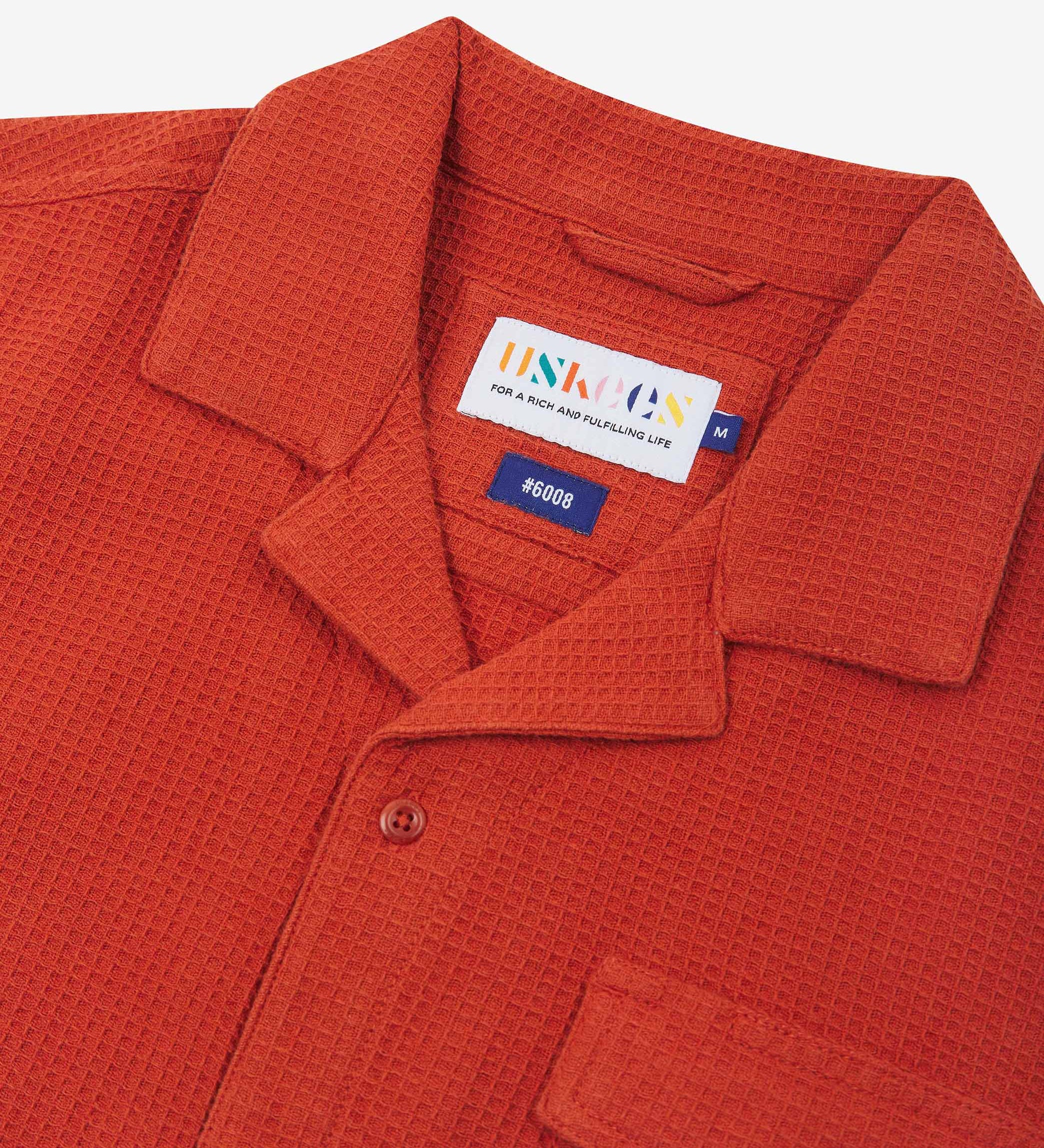 Close-up view of the #6008 shirt collar, showing weave of rust-red organic cotton waffle fabric, camp notched collar and Uskees branding label.