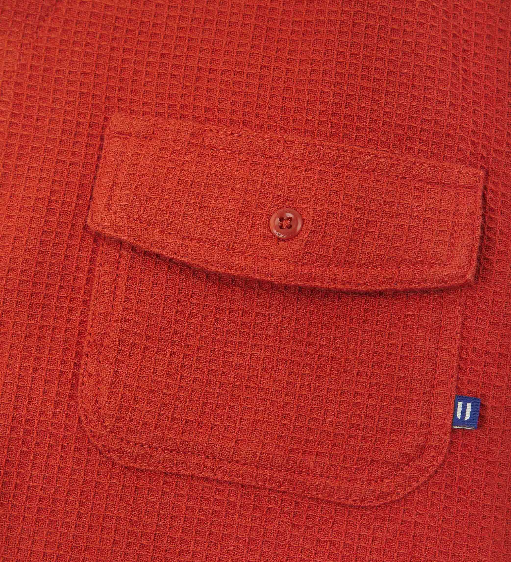 Close-up view of #6008 Uskees buttoned organic cotton waffle fabric short sleeve shirt in rust-red with focus on button down flap pocket on chest and the subtle Uskees branding tag.