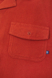 Close-up view of #6008 Uskees buttoned organic cotton waffle fabric short sleeve shirt in rust-red with focus on button down flap pocket on chest and the subtle Uskees branding tag.