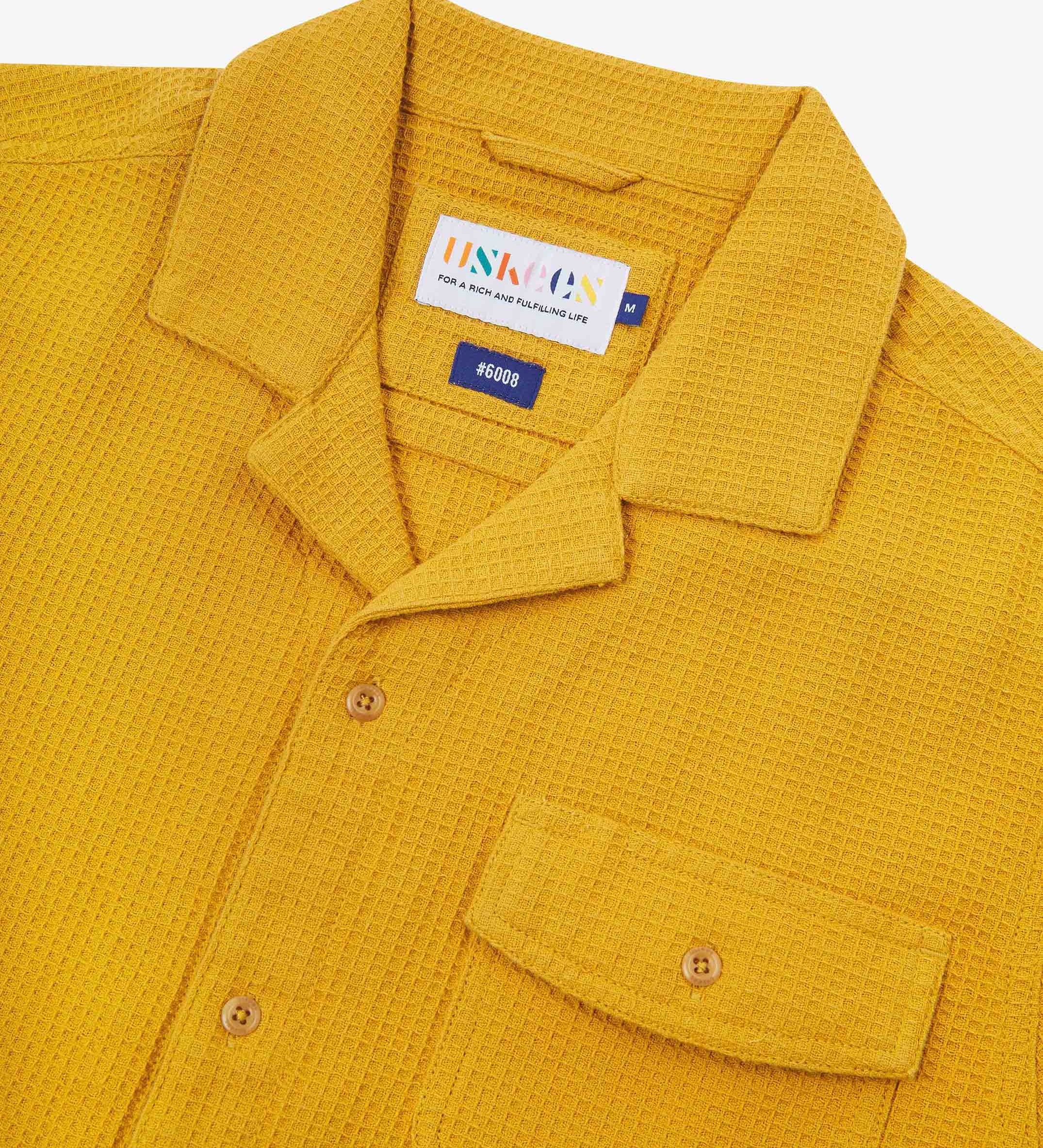 Close-up view of the #6008 shirt collar, showing weave of yellow organic cotton waffle fabric, camp notched collar and Uskees branding label.