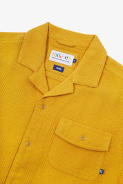 Close-up view of the #6008 shirt collar, showing weave of yellow organic cotton waffle fabric, camp notched collar and Uskees branding label.