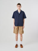 Full-length front view of model wearing an Uskees dark blue Cuban shirt paired with khaki shorts.