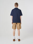 Full-length back view of model wearing an Uskees dark blue Cuban shirt paired with khaki shorts.