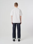 Full-length back view of model wearing an Uskees off-white Cuban shirt paired with indigo raw orta Uskees jeans.