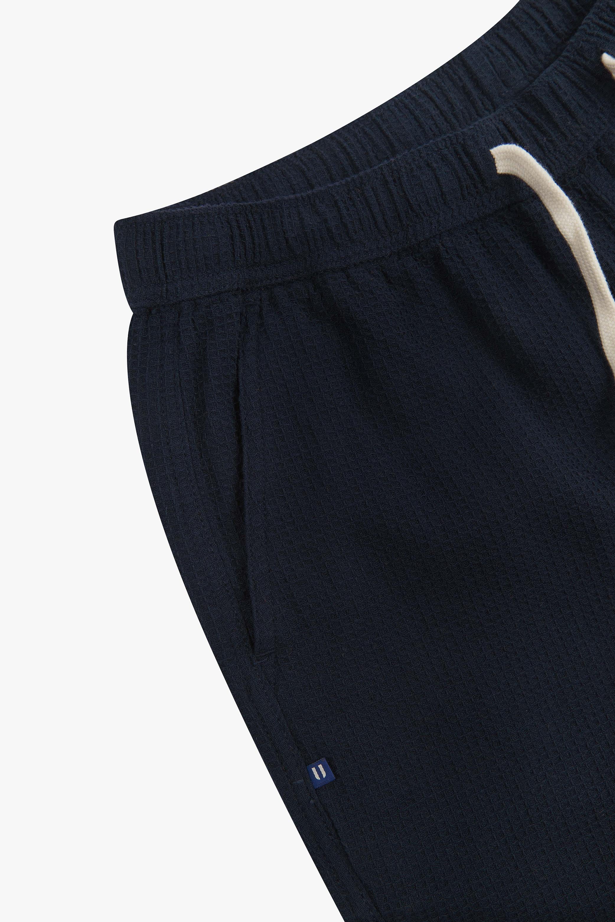 Close-up angled view of a side pocket, elasticated waist and drawstring of the casual deep-blue waffle cotton shorts.