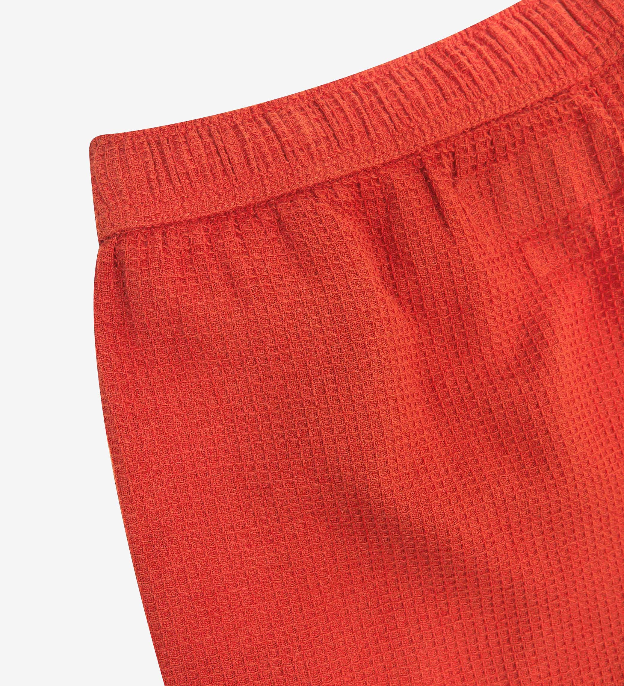 Close-up angled rear view of the #6009 Uskees shorts, presenting a closer view of the elasticated waistband and rust-red waffle fabric.