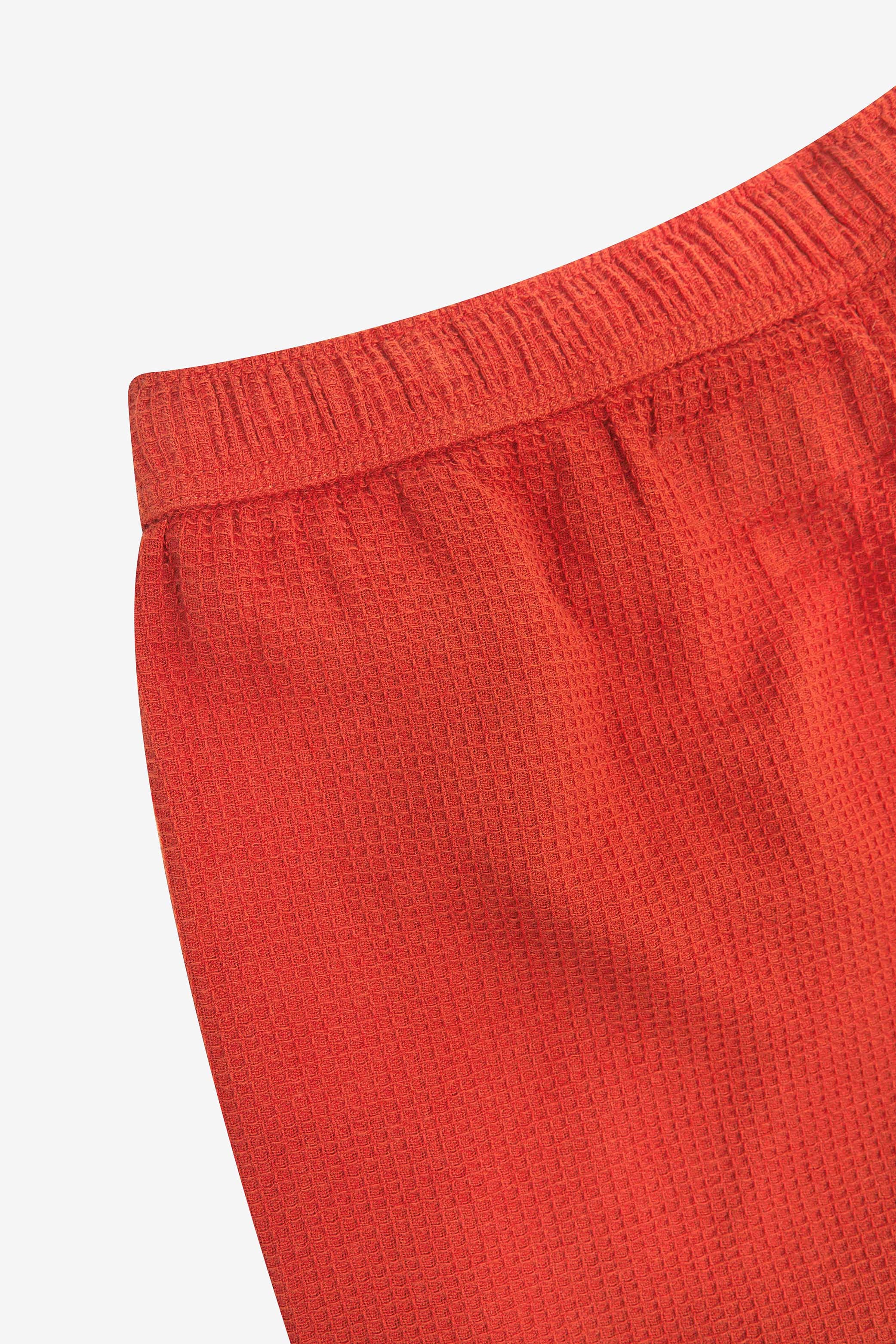 Close-up angled rear view of the #6009 Uskees shorts, presenting a closer view of the elasticated waistband and rust-red waffle fabric.