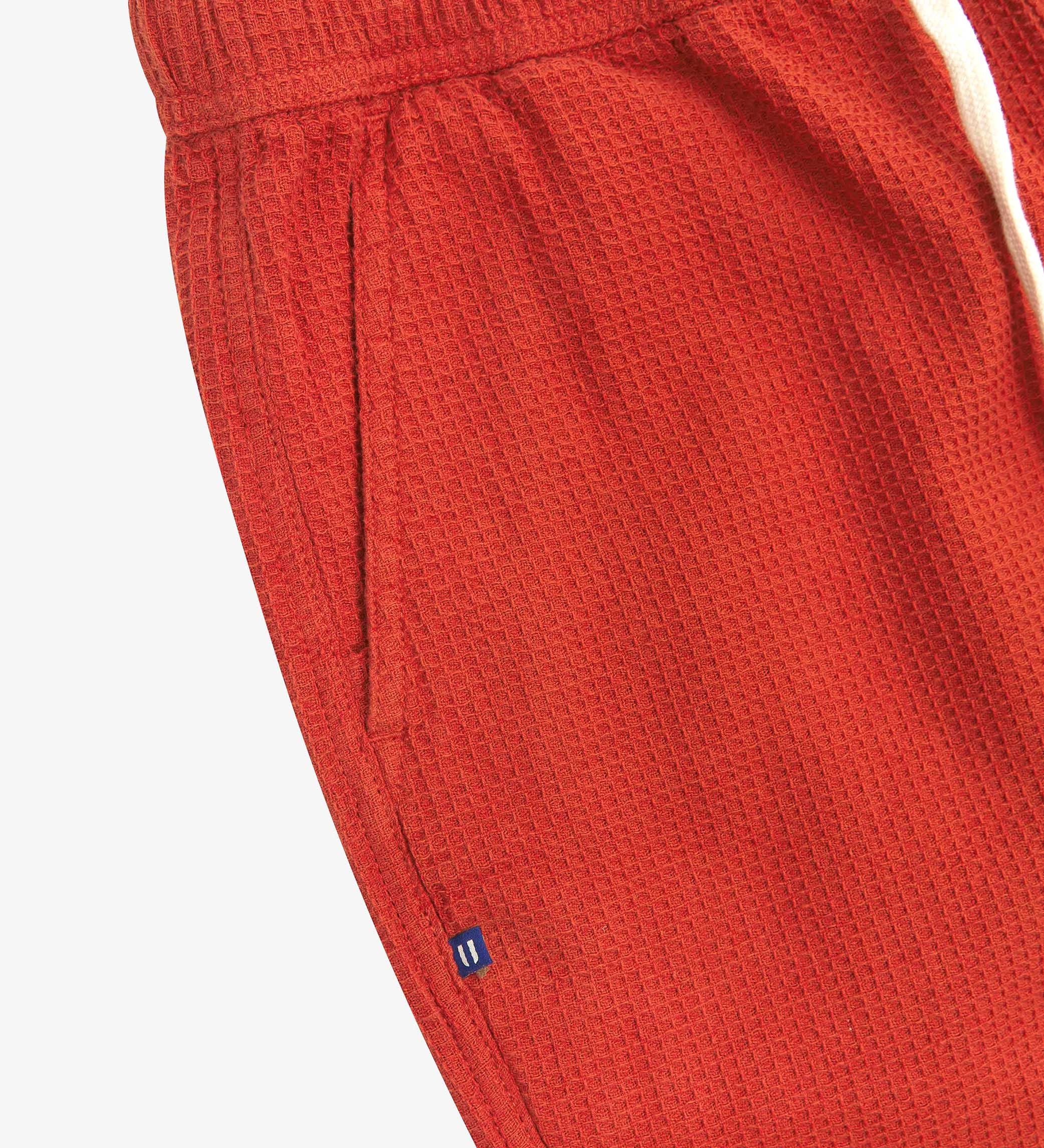 Close-up angled view of a side pocket, elasticated waist and drawstring of the casual rust-red waffle cotton shorts.