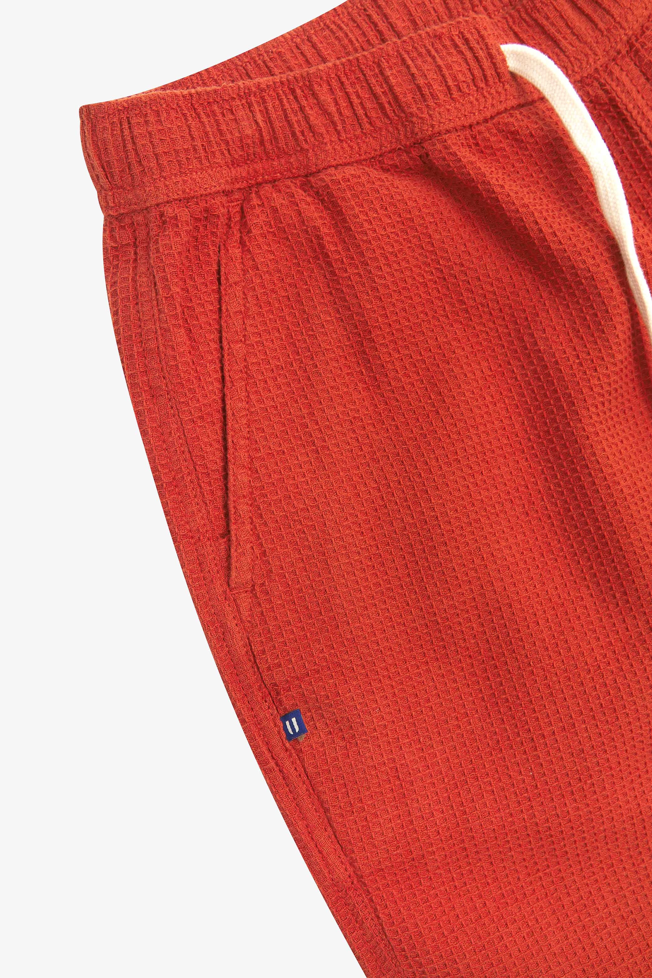 Close-up angled view of a side pocket, elasticated waist and drawstring of the casual rust-red waffle cotton shorts.