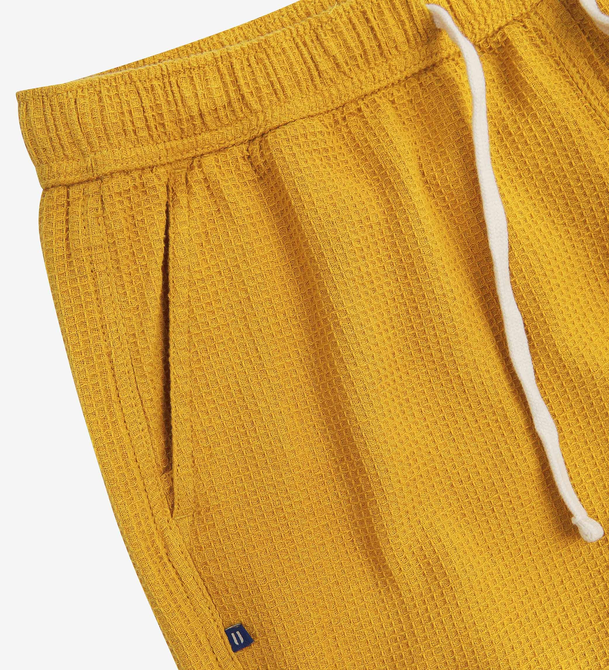 Close-up angled view of a side pocket, elasticated waist and drawstring of the casual yellow waffle cotton shorts.