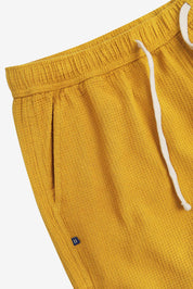 Close-up angled view of a side pocket, elasticated waist and drawstring of the casual yellow waffle cotton shorts.