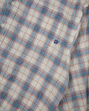 Close-up of an Uskees blue pebble plaid lumberjack shirt with small blue brand logo tab on the pocket. 