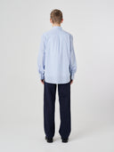 Full-length back view of man wearing Uskees blue, gold and white striped men's Oxford shirt.