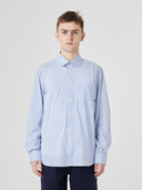 Top-half view of man wearing Uskees blue, gold and white striped men's Oxford shirt, paired with Uskees dark pants.