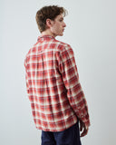 A man wearing an Uskees red and white plaid long-sleeve button-up method shirt, shown from a side-back angle against a plain light gray studio background.