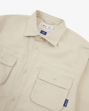 Close up flat shot of an Uskees beige long sleeved shirt for men showing the chest pocket and collar detail.