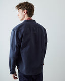 A male model wearing a dark navy blue long-sleeve button-up overshirt, shown from the back against a plain light gray studio background.