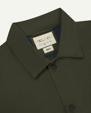 front detail flat shot of uskees dark green oversized coach jacket showing front popper fastening and neck label