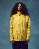 Front view wearing the Uskees wax storm jacket in British yellow. Jacket fastened, clearly showing the large flap pockets and secured storm collar.