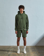 Full-length front view of model wearing coriander green organic cotton #7004 jersey, drawstring-hooded sweater with front pouch pocket.