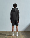 Full-length back view of model wearing faded black, relaxed cut organic cotton #7004 jersey sweater. Showing hood, ribbed cuffs and hem.