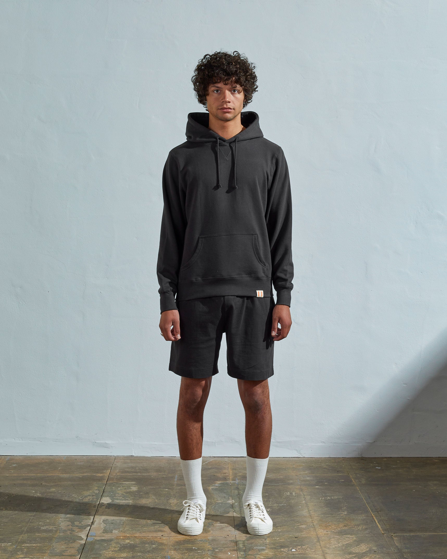 Full-length front view of model wearing faded black organic cotton #7004 jersey hooded sweater with front pouch pocket.
