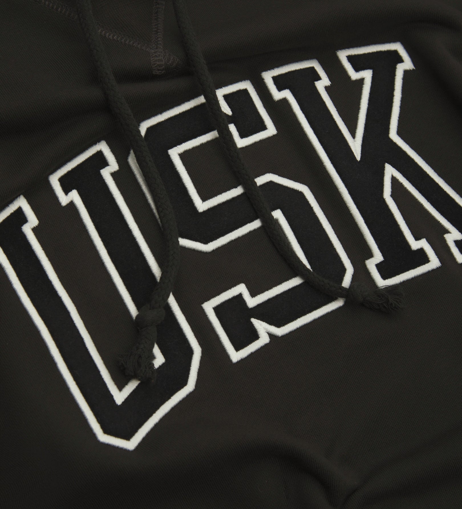 Front close up shot of Uskees signature faded black men's hooded sweatshirt showing the 'USK' logo detail.