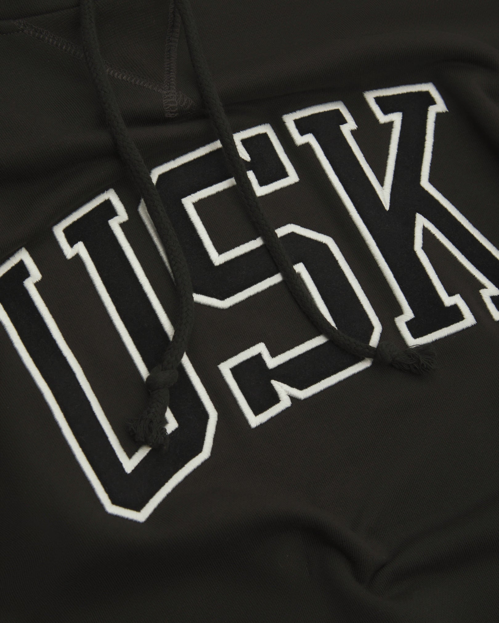 Front close up shot of Uskees signature faded black men's hooded sweatshirt showing the 'USK' logo detail.