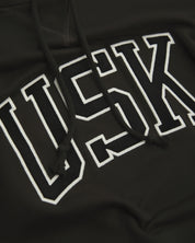 Front close up shot of Uskees signature faded black men's hooded sweatshirt showing the 'USK' logo detail.