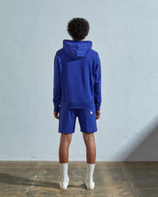 Full-length back view of model wearing 'ultra blue', relaxed cut organic cotton 7004 jersey sweater. Showing hood, ribbed cuffs and hem.
