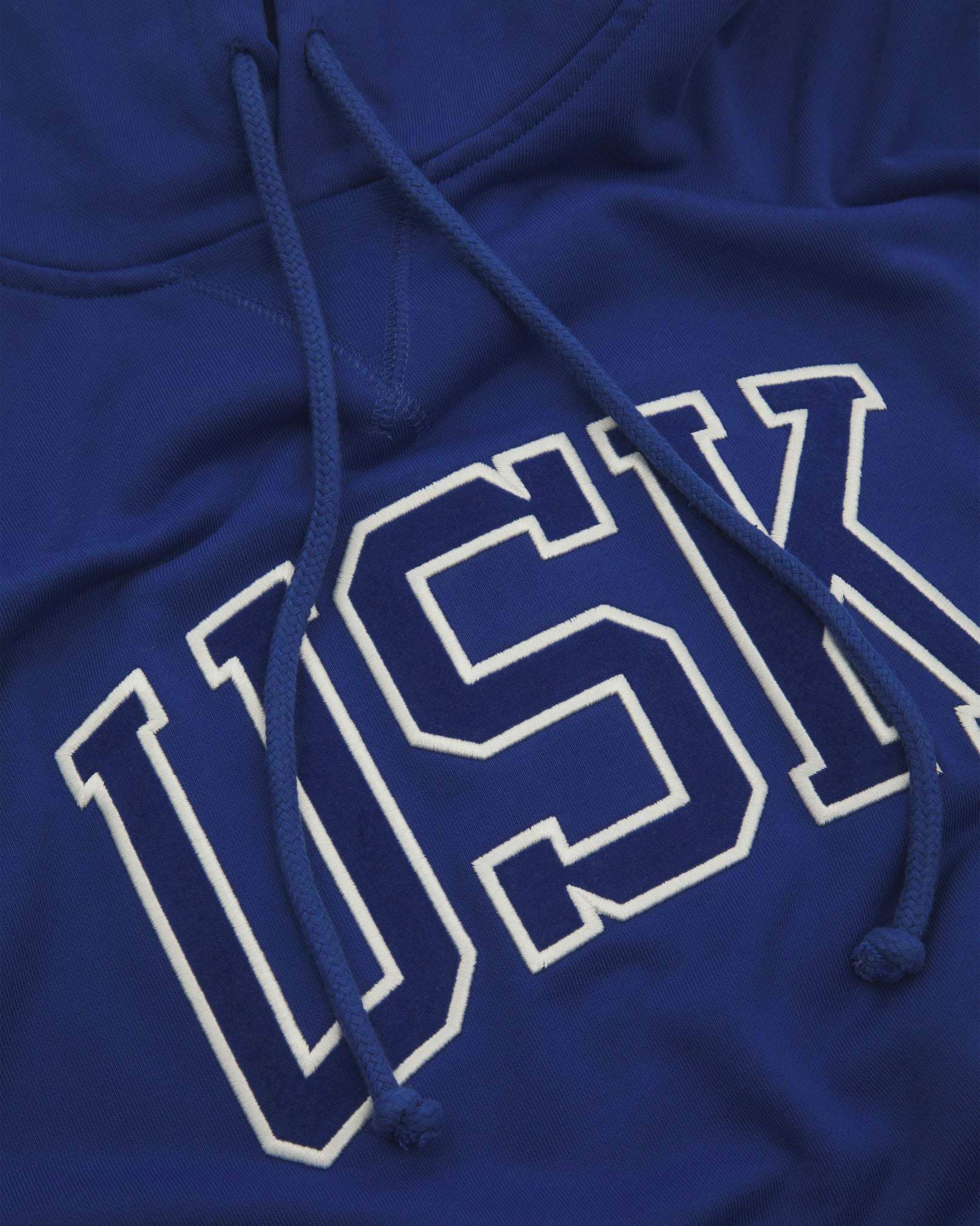 Front close shot of Uskees signature ultra blue men's hooded sweatshirt showing the 'USK' logo and hood drawstrings.