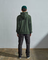 Full-length back view of model wearing vine green, relaxed cut organic cotton #7004 jersey sweater. Showing hood, ribbed cuffs and hem.