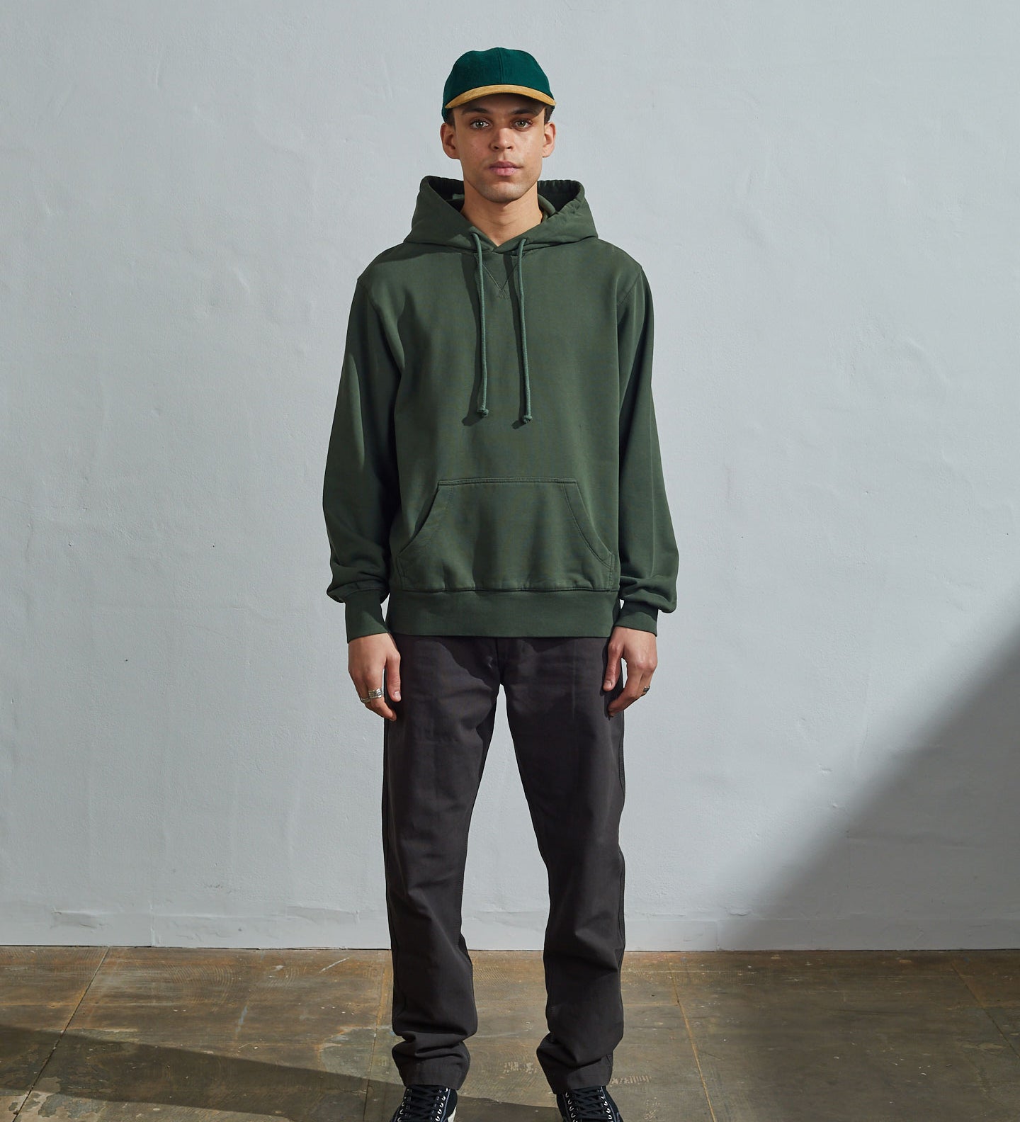 Full-length front view of model wearing vine green organic cotton #7004 jersey hooded sweater with front pouch pocket.