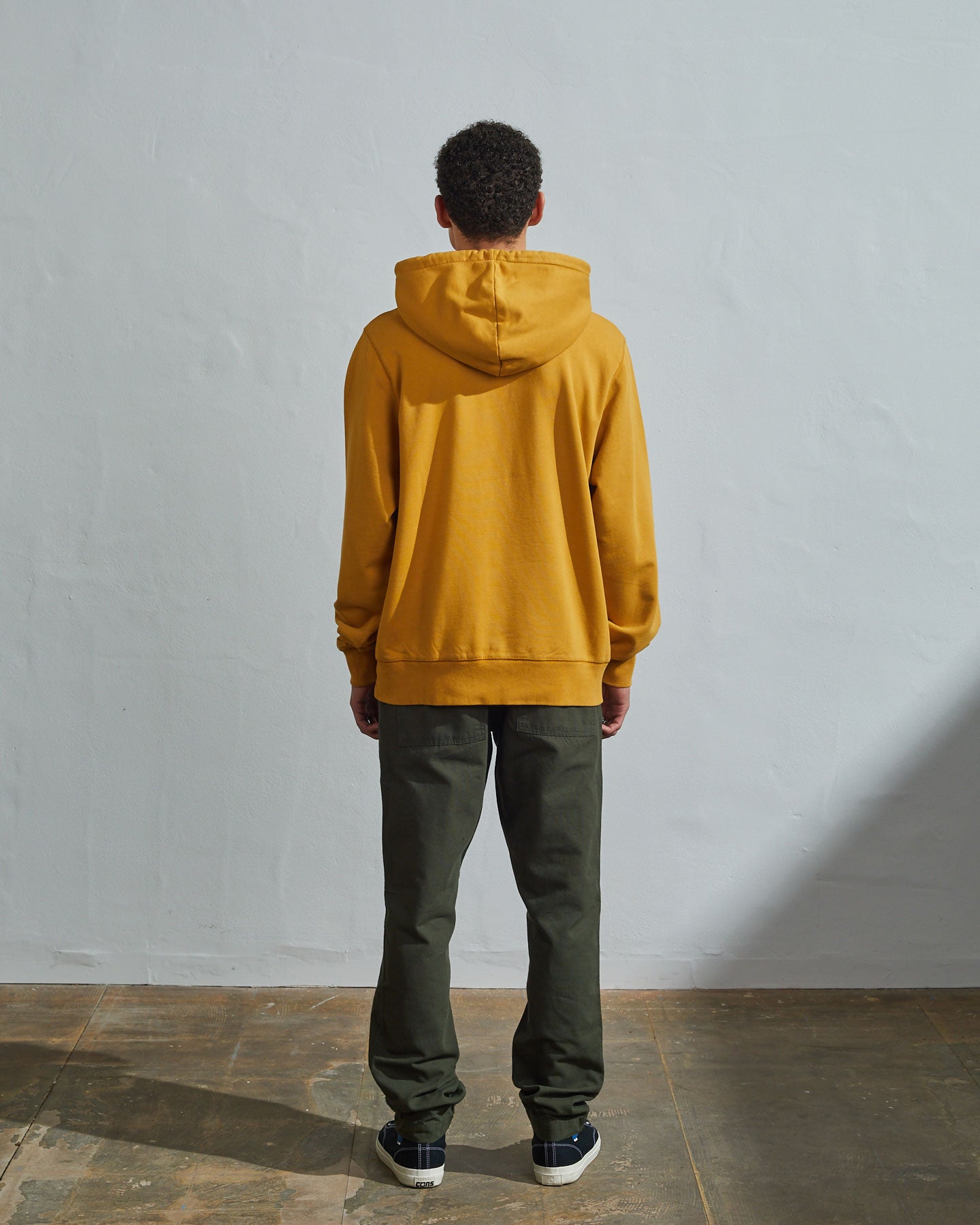Full-length back view of model wearing yellow, relaxed cut organic cotton #7004 jersey sweater. Showing hood, ribbed cuffs and hem.