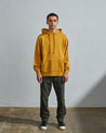 Full-length front view of model wearing yellow organic cotton #7004 jersey hooded sweater with front pouch pocket.