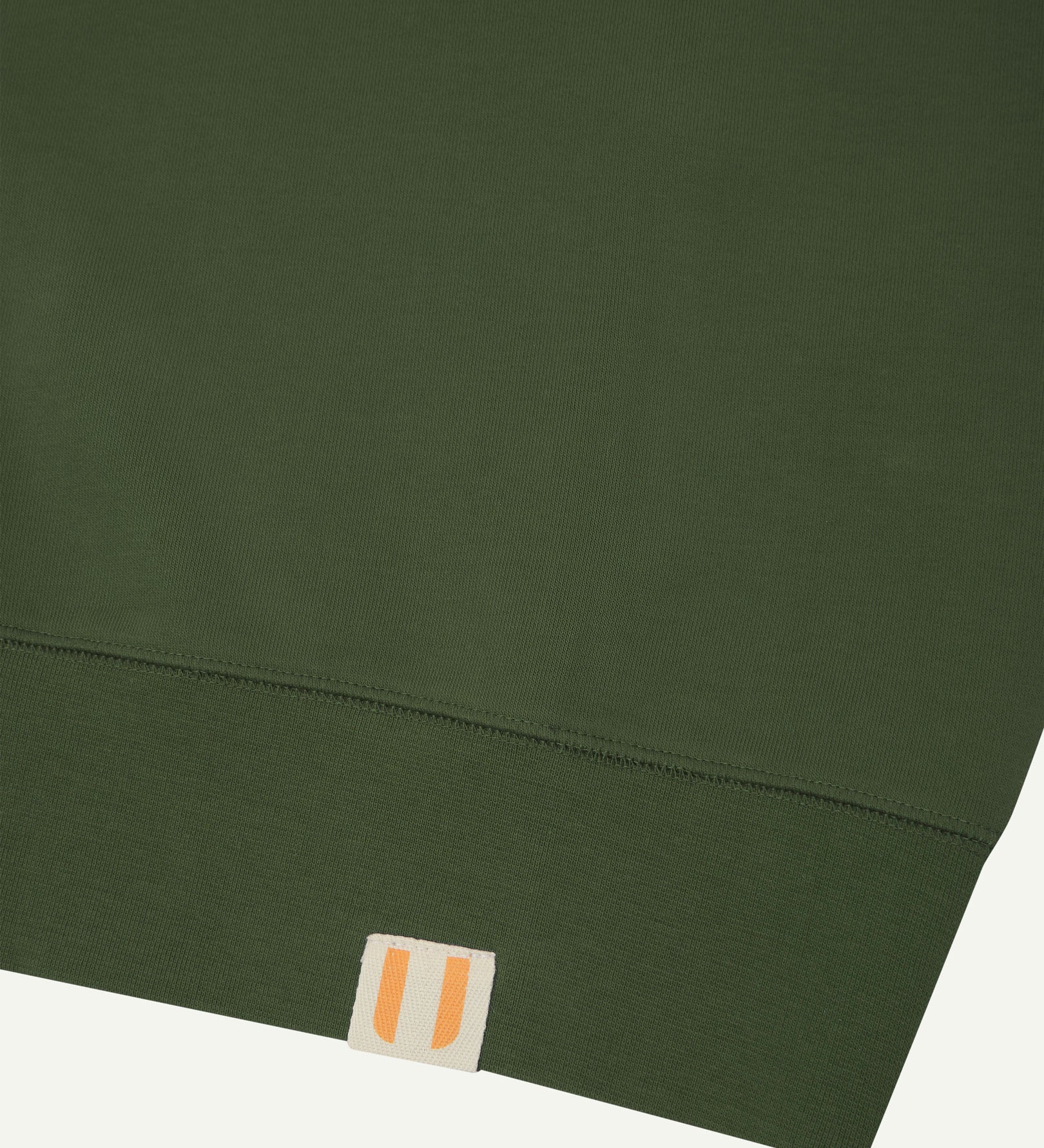 Closer view view of the discreet brand logo on ribbed hem of the Uskees coriander-green organic heavyweight cotton 7005 jersey sweatshirt.
