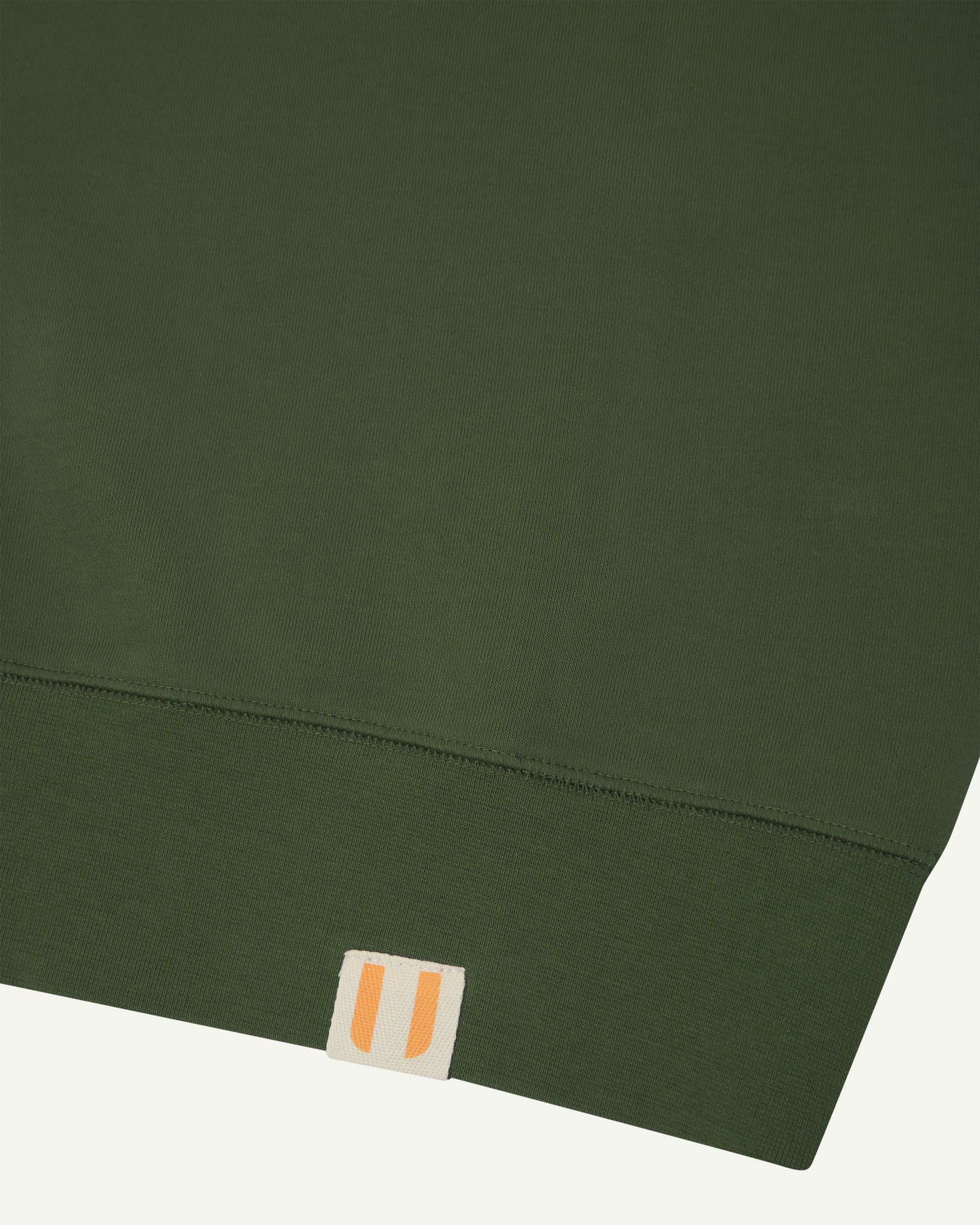 Closer view view of the discreet brand logo on ribbed hem of the Uskees coriander-green organic heavyweight cotton 7005 jersey sweatshirt.