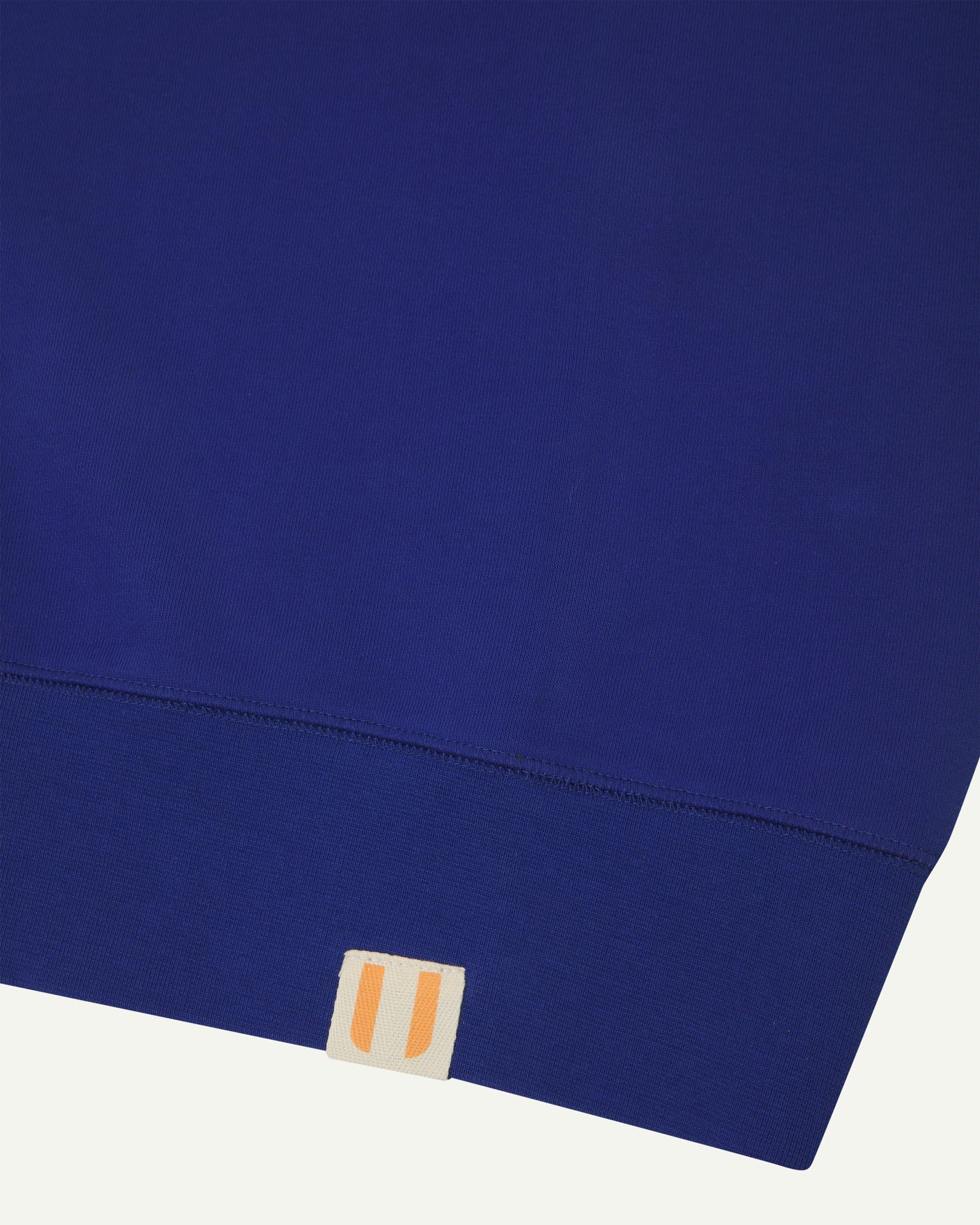 Closer view view of the discreet brand logo on ribbed hem of the Uskees ultra-blue organic heavyweight cotton 7005 jersey sweatshirt.