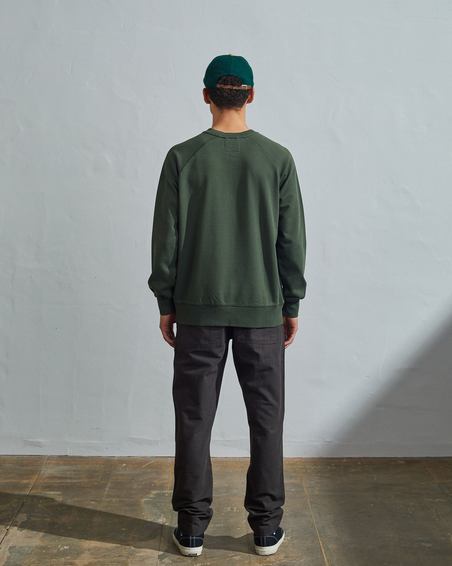 Full-length back view of model wearing vine green, relaxed cut organic cotton #7005 jersey sweatshirt with ribbed cuffs and hem.