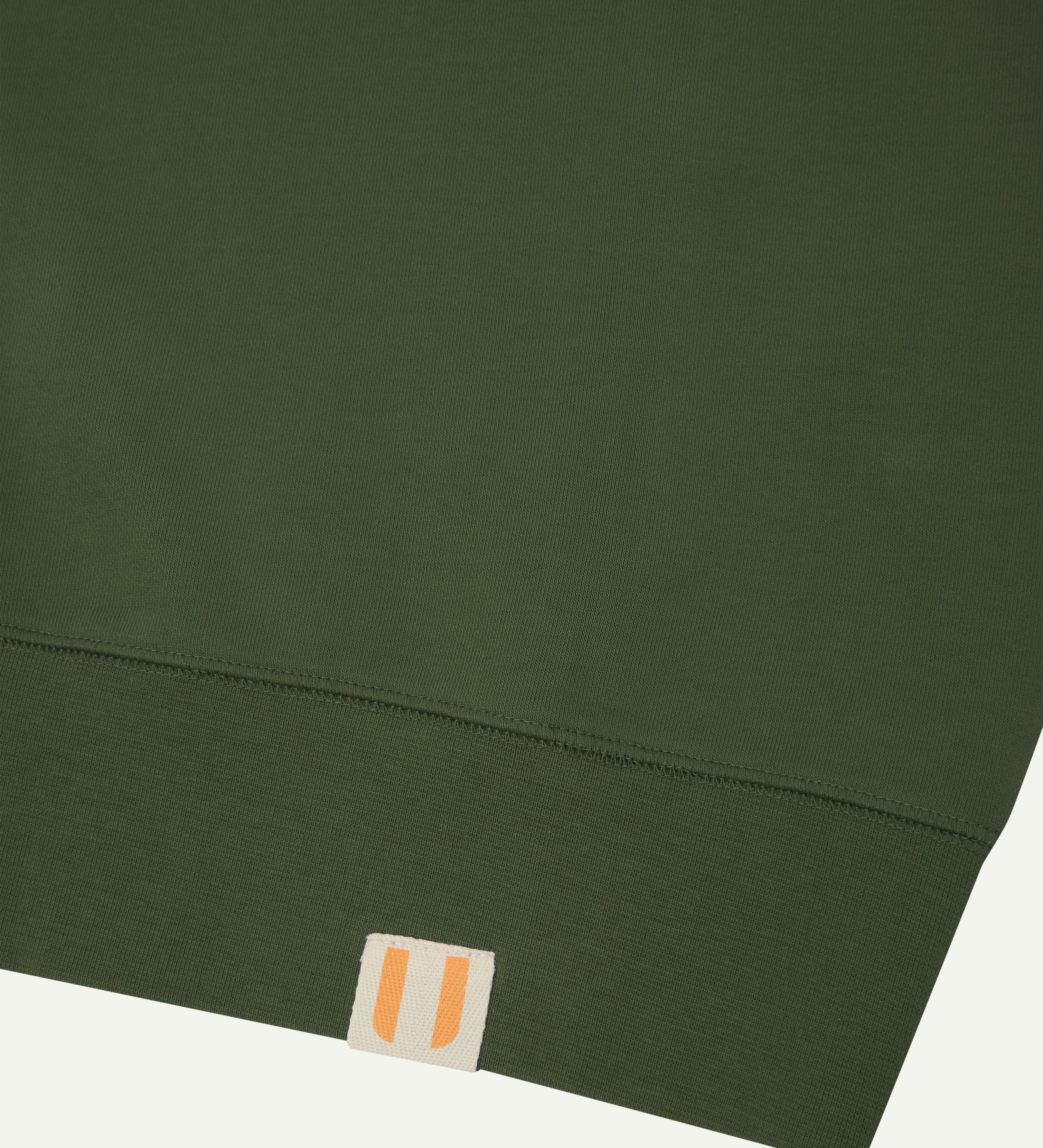 Close-up view of vine green organic heavyweight cotton #7005 jersey sweatshirt by Uskees showing brand logo at hem.