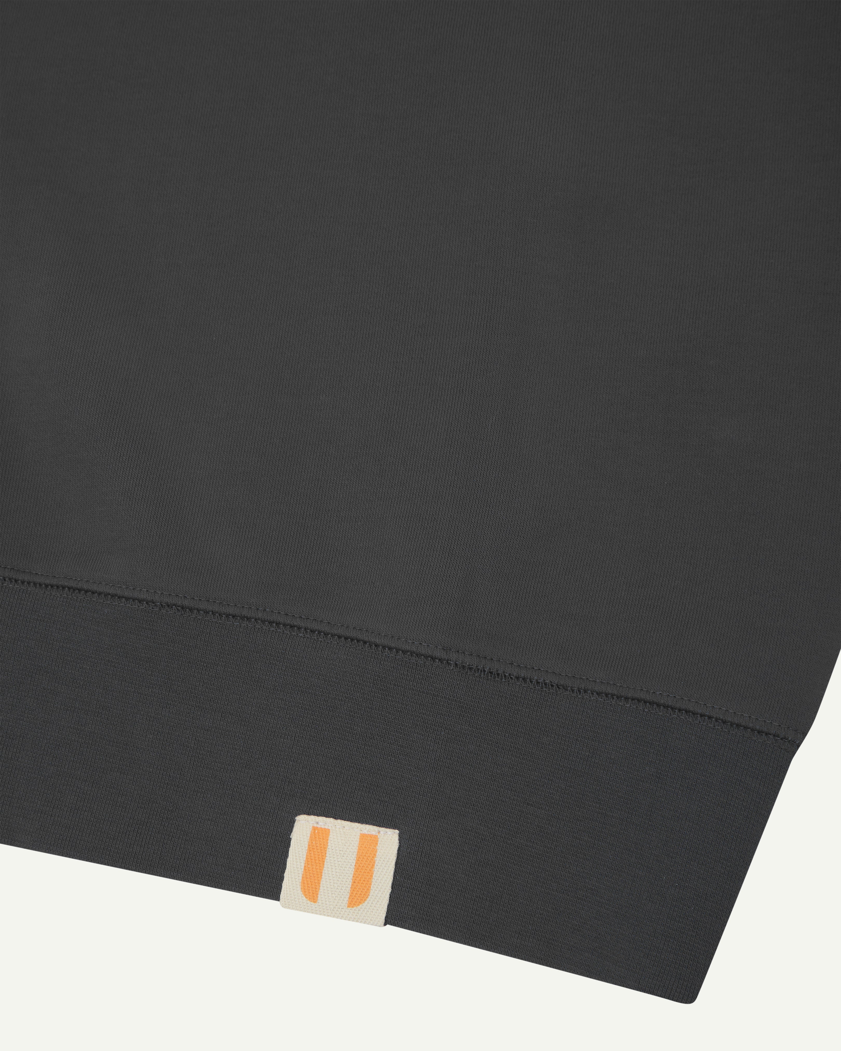 Close-up view of hem showing uskees logo label - dark grey organic heavyweight cotton #7005 sweatshirt for men.
