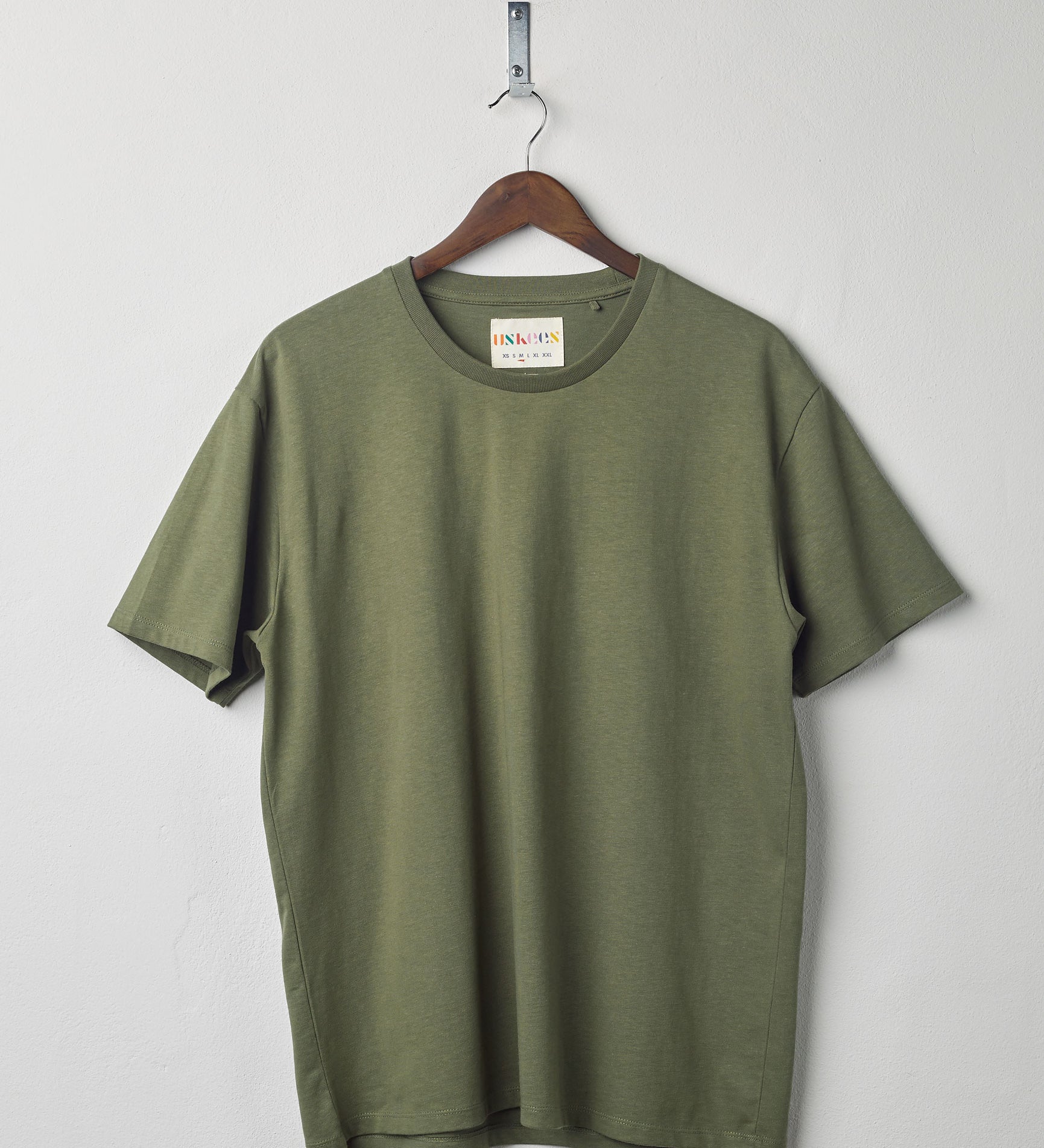 Front view of army green organic cotton #7006 jersey T-shirt by Uskees, presented on hanger against white background. 