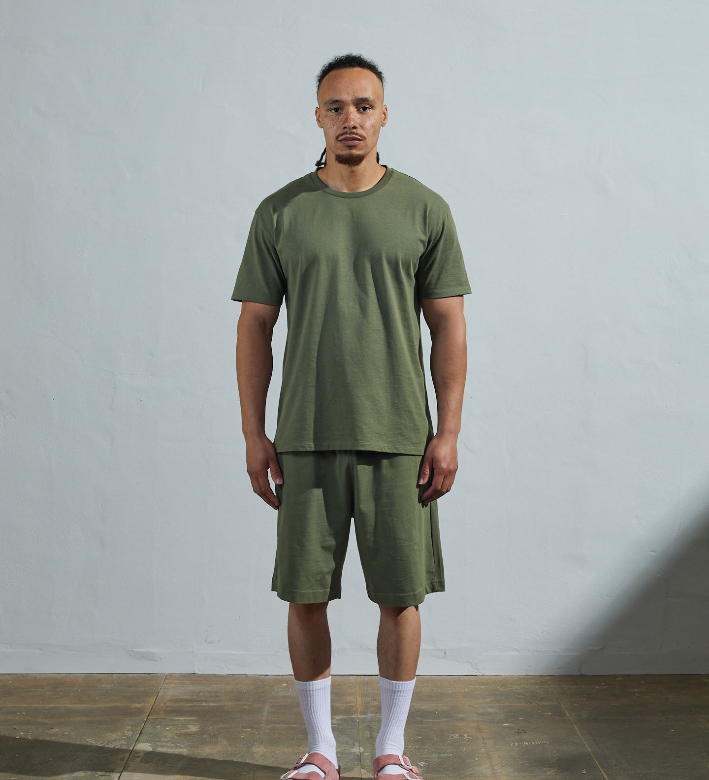 Full-length front view of model wearing army green organic cotton #7006 jersey T-shirt by Uskees paired with matching #7007 shorts.