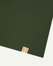 Hem close-up of Uskees coriander green organic cotton T-shirt showing square branding label.