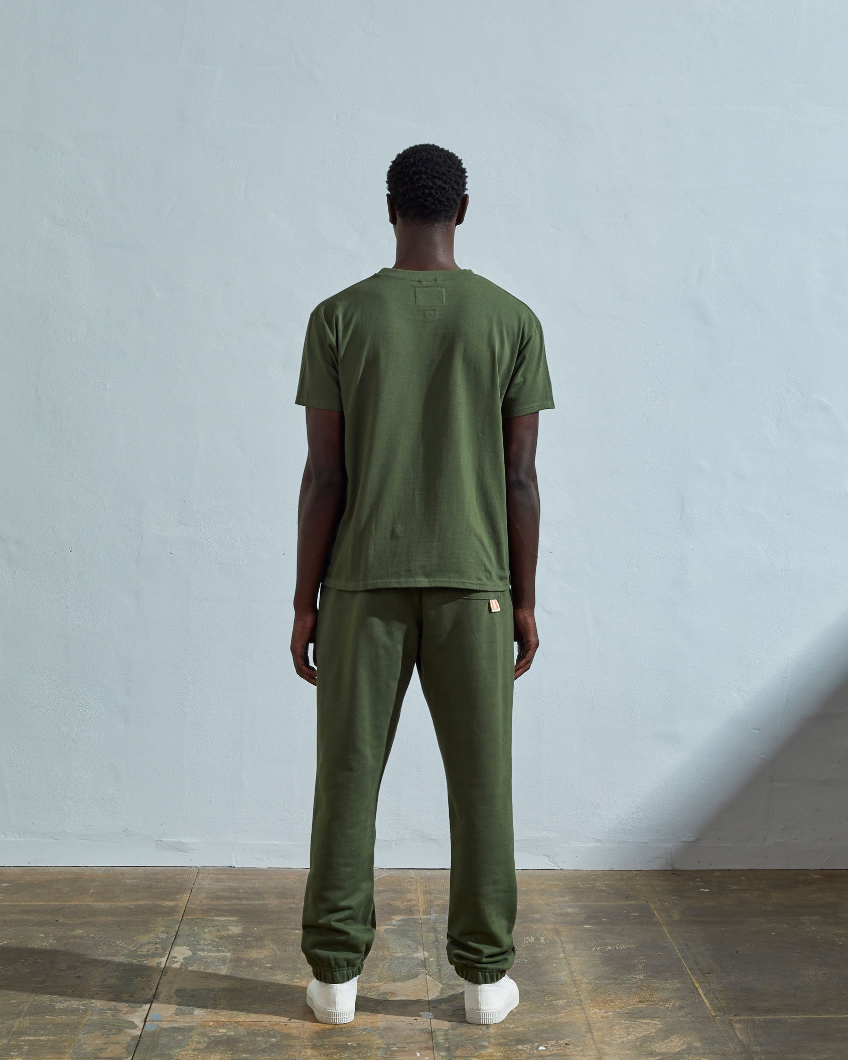 Full-length back view of model wearing coriander-green, relaxed cut organic cotton #7006 jersey T-shirt by Uskees paired with matching pants.