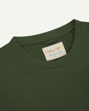 Neckline close-up of Uskees coriander green organic cotton T-shirt showing hanging loop and branding label.